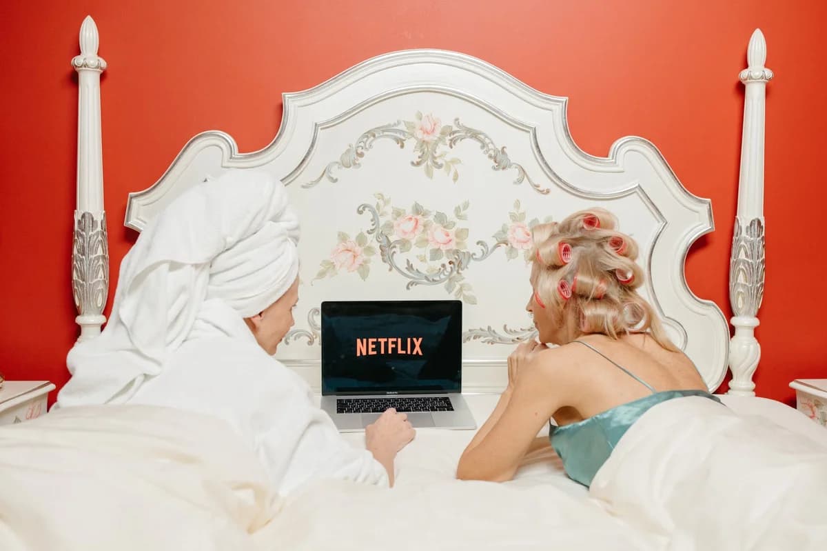 Two women on a bed watching Netflix on a laptop in a red vintage-style bedroom
