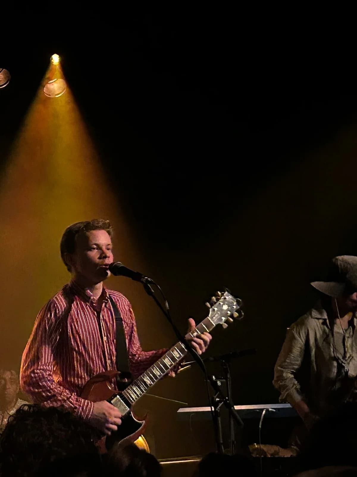 Geordie Greep performing on stage with a guitar under a spotlight.