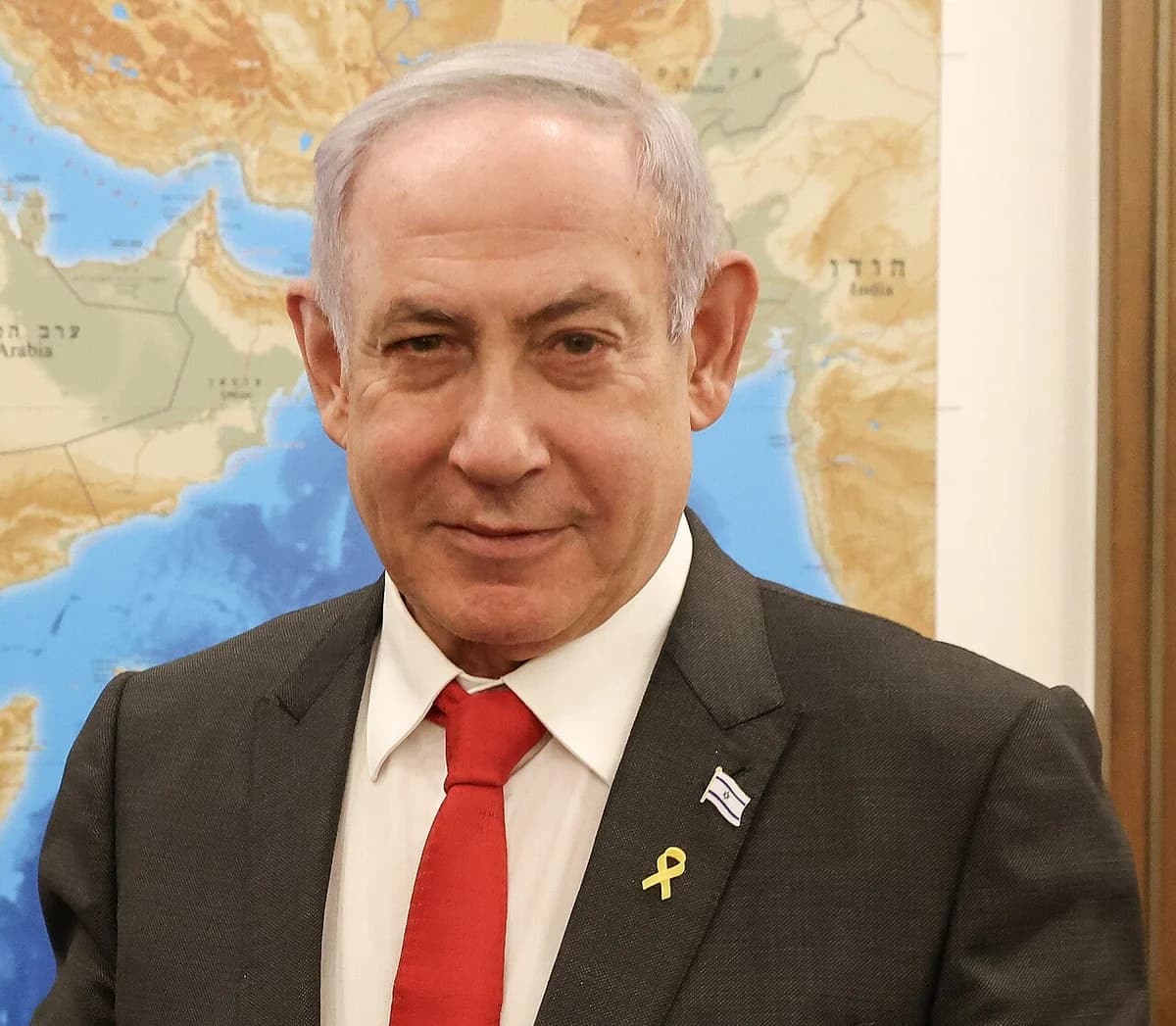 Benjamin Netanyahu in a suit and red tie in front of a map background.