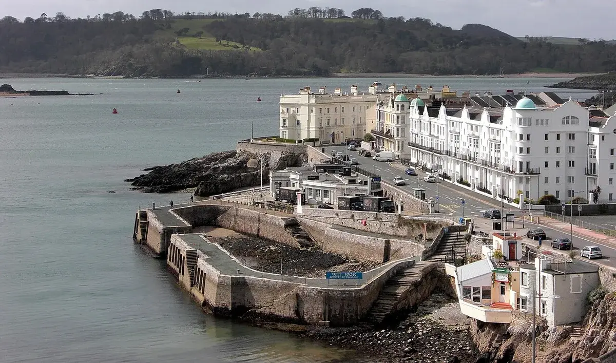 A small dock and waterfront buildings along the calm coast at Plymouth Hoe.
