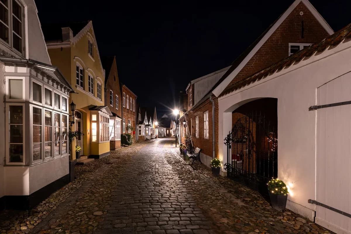 A narrow cobblestone street in Tønder, Denmark, at night with historic houses lining both sides.