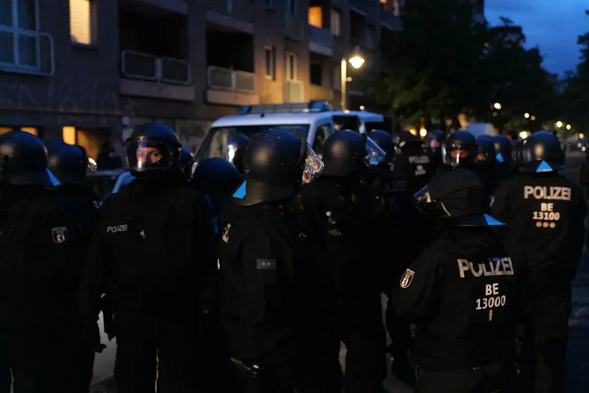 Police officers in riot gear gathered on a street at dusk during a protest.