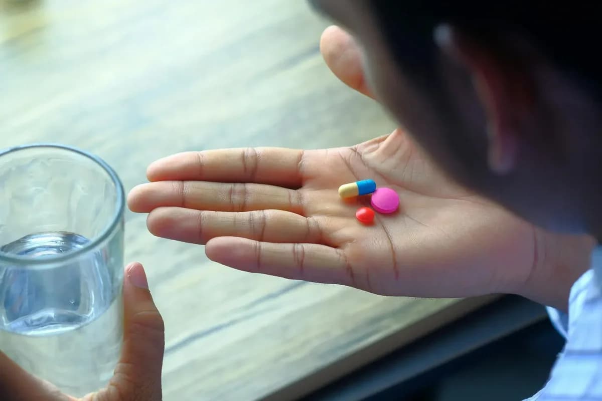 Hand holding pills with glass of water