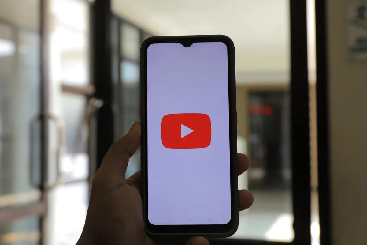 Hand holding a smartphone showing the YouTube app logo indoors