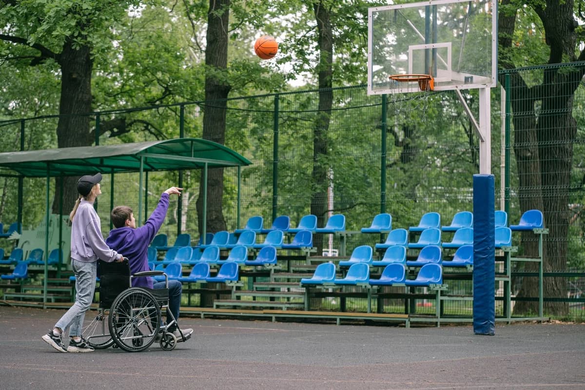 Two people playing basketball outdoors, one in a wheelchair.