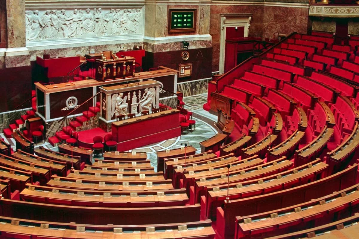 Empty parliamentary chamber with red seats and ornate wall decorations.