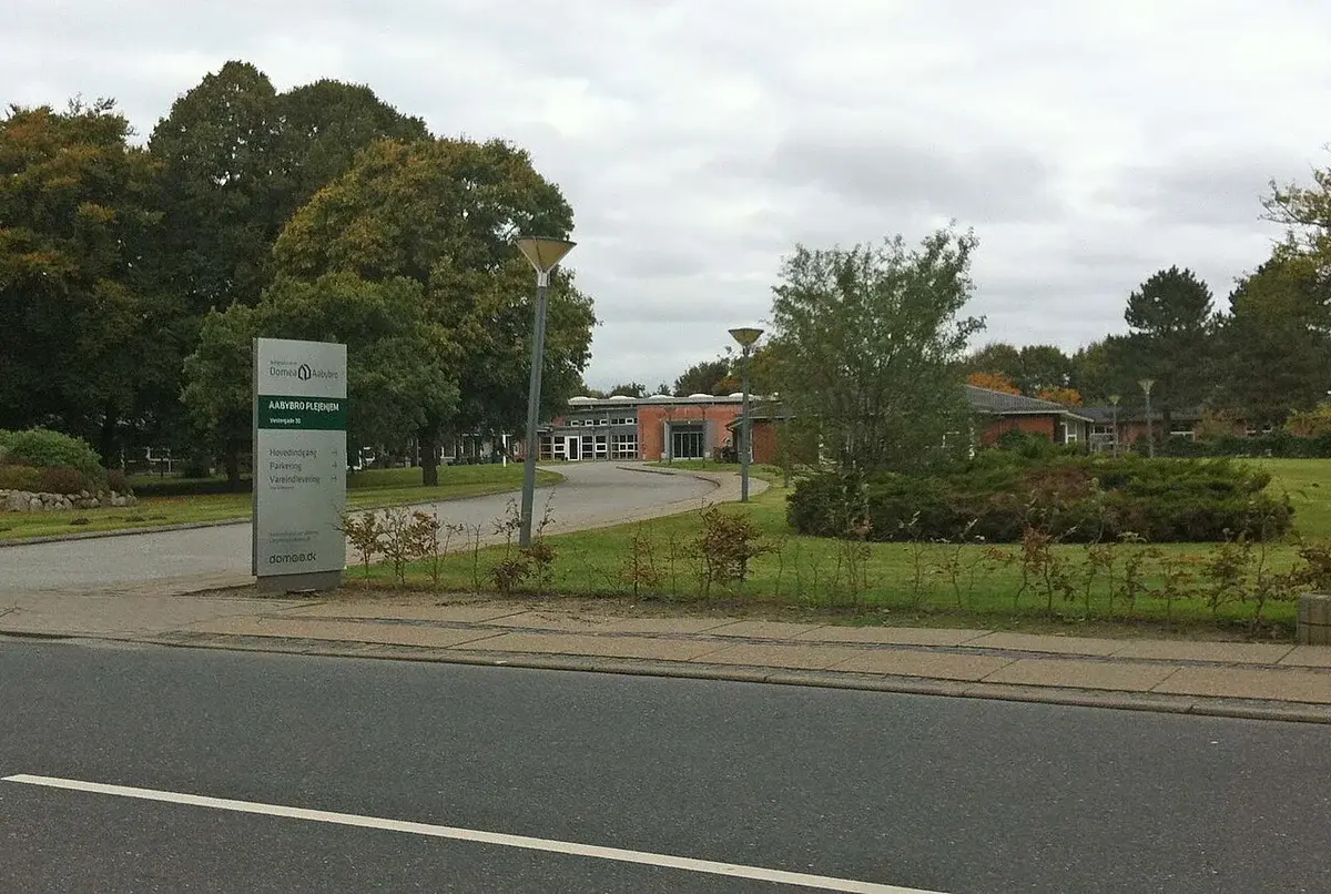 Entrance sign for Aabybro Nursing Home beside a driveway and landscaped grounds.