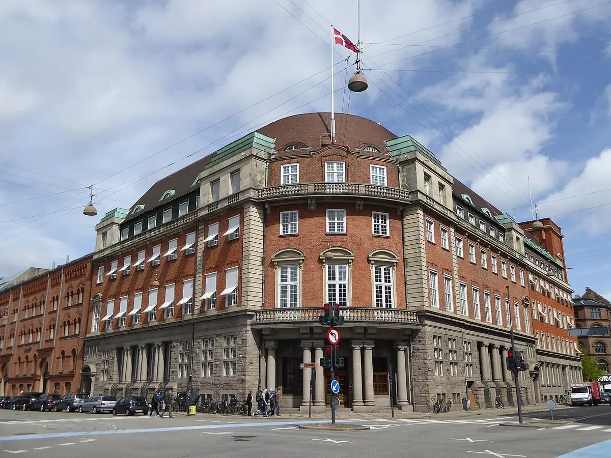 Historic brick building at a Copenhagen street corner with a Danish flag on the roof.