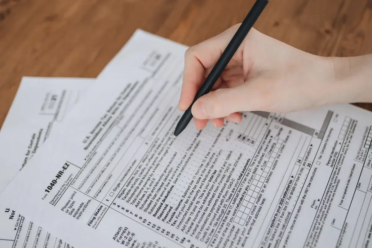 A hand writing on tax forms with a black pen.