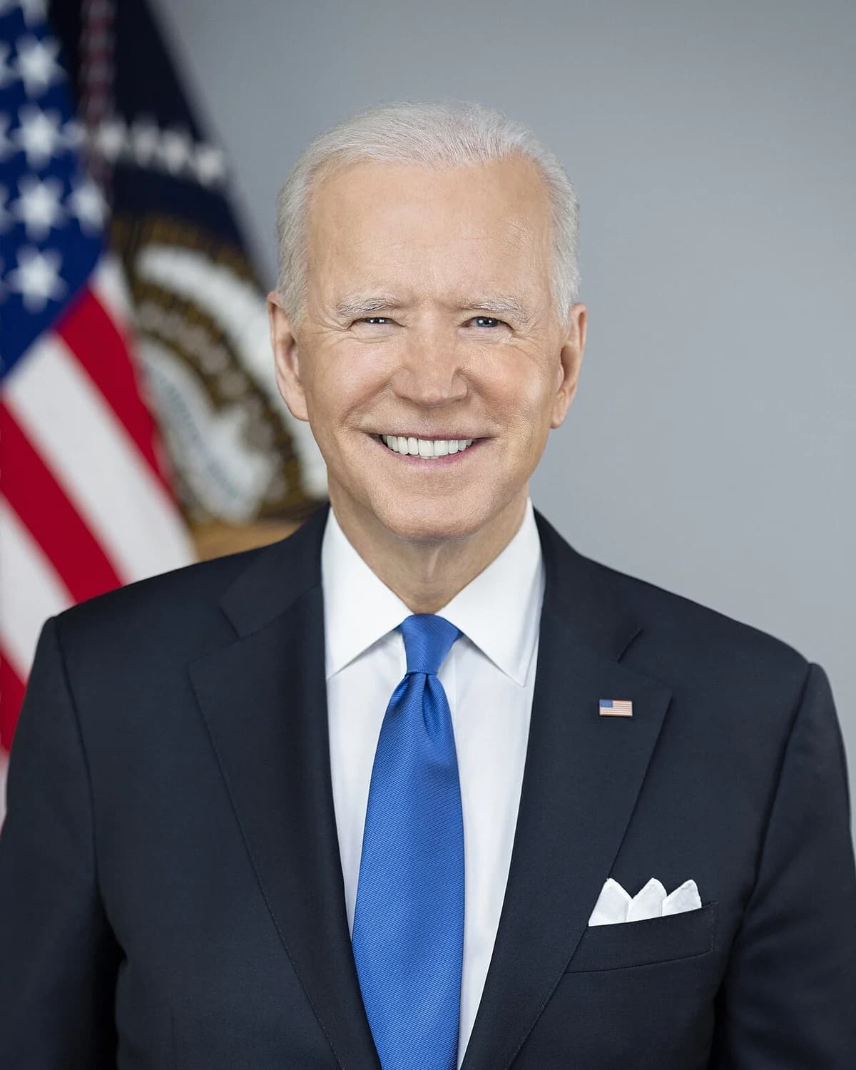 Portrait of President Joe Biden in a suit with an American flag behind him.