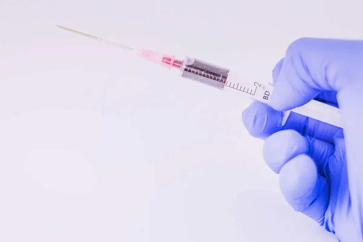A gloved hand holding a syringe with a needle.