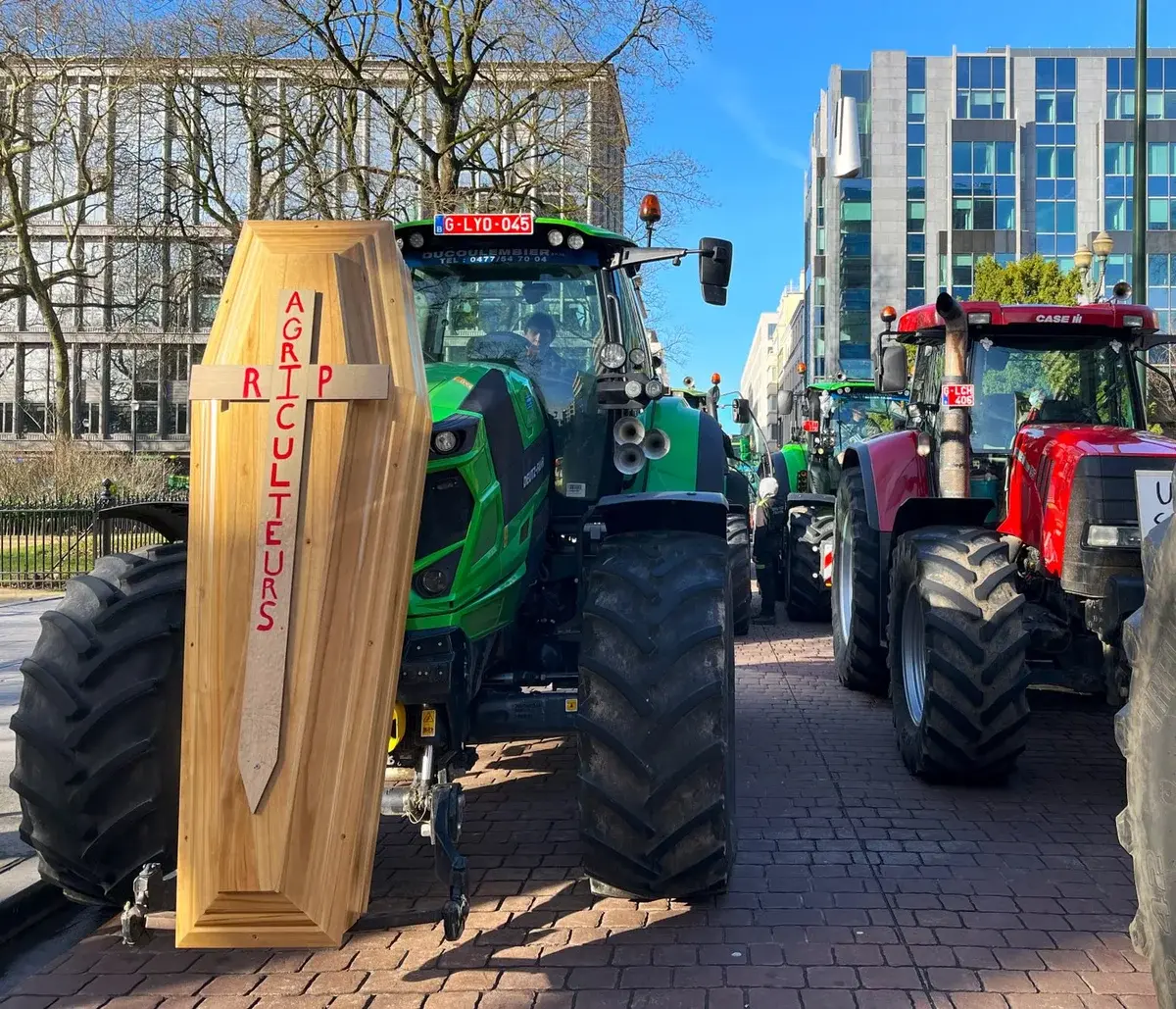 Tractors lined up in city protest with wooden coffin saying RIP AGRICULTEURS