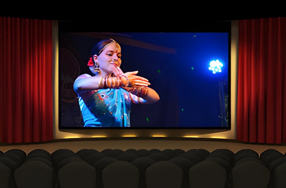 A movie theater with a screen showing a woman performing a dance.