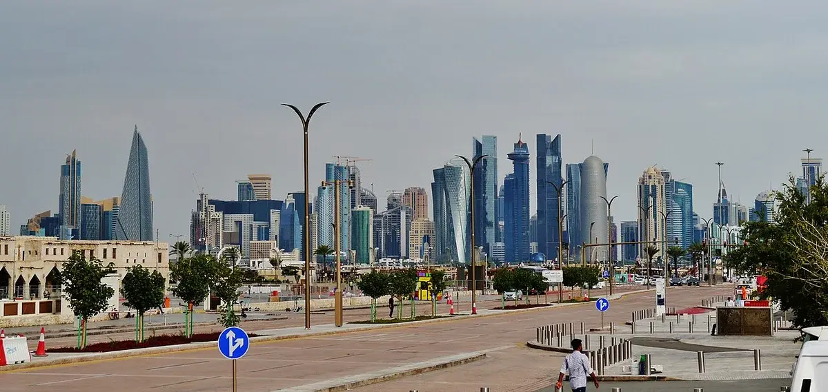 Modern skyline of Doha, Qatar, seen from a road with streetlights in the foreground.