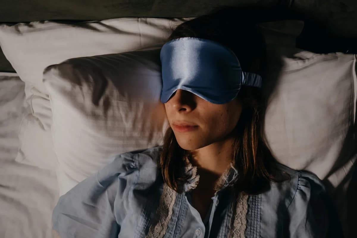 Woman lying in bed wearing a blue sleep mask.