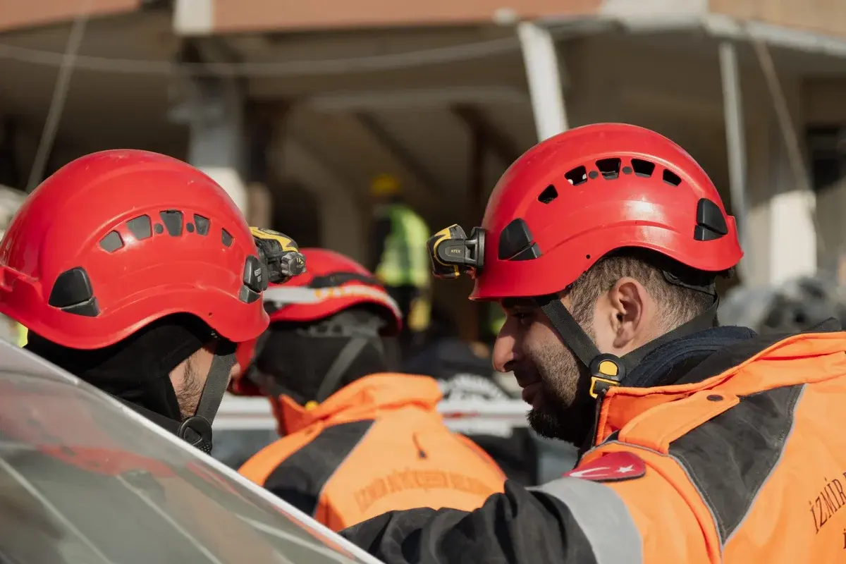 Rescue workers in red helmets and orange jackets collaborate during an emergency operation.