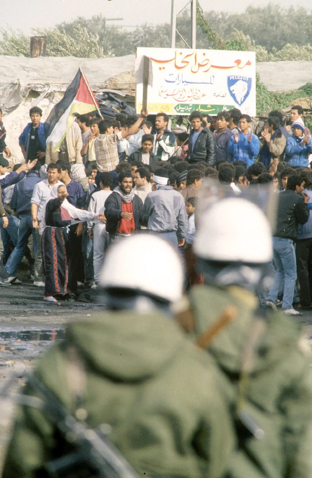 Palestinian protesters gathered during an intifada with security forces in the foreground.