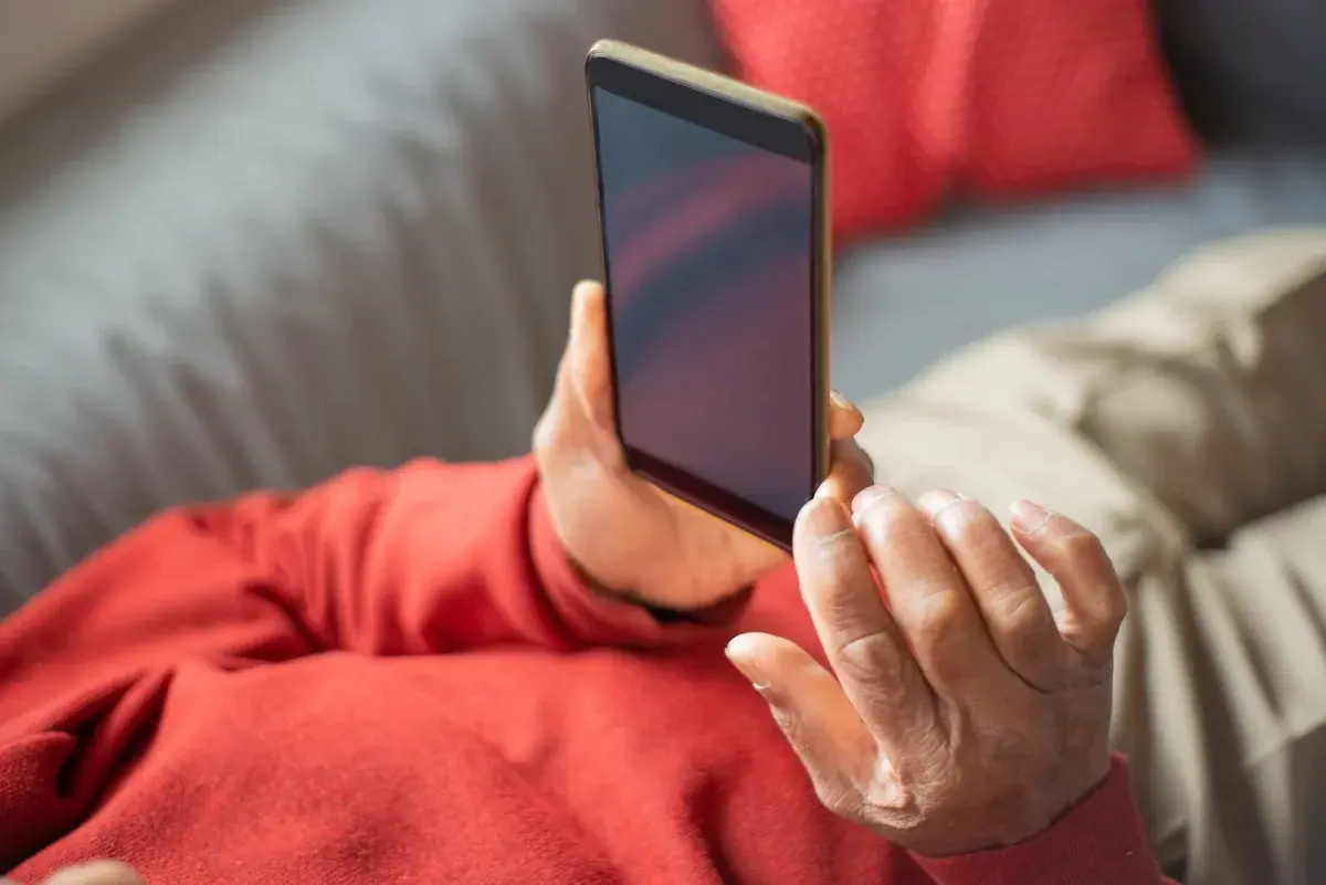An older adult holding a smartphone while sitting indoors.