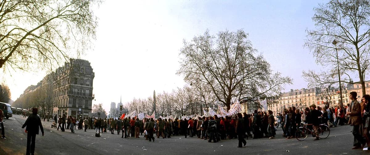 Crowd of students protesting on a Paris street with banners and flags.