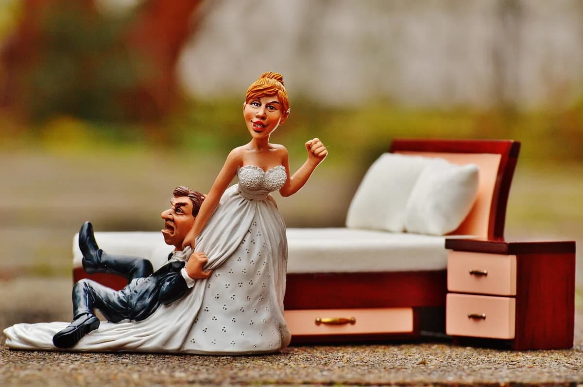 A stylized bride and groom figurine beside a bed.