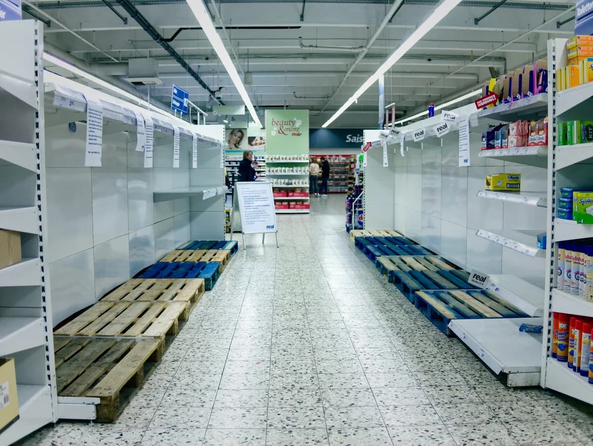 Mostly empty supermarket shelves in an aisle with a few products left.