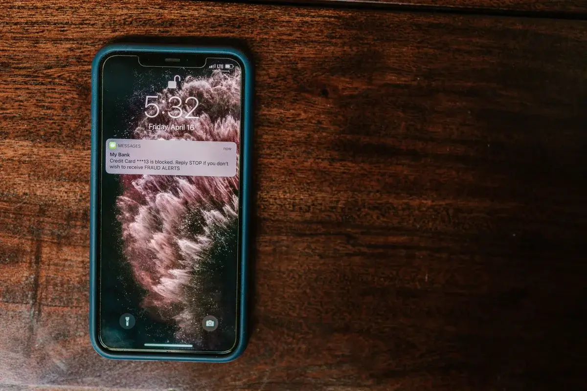 A smartphone on a wooden table displays a bank alert about a blocked credit card.