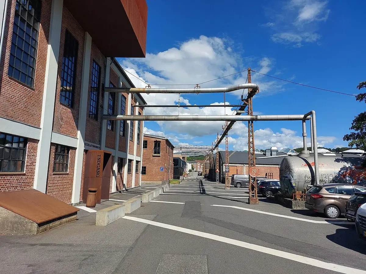 Street view of Spinderigade in Vejle with industrial buildings and overhead pipes.