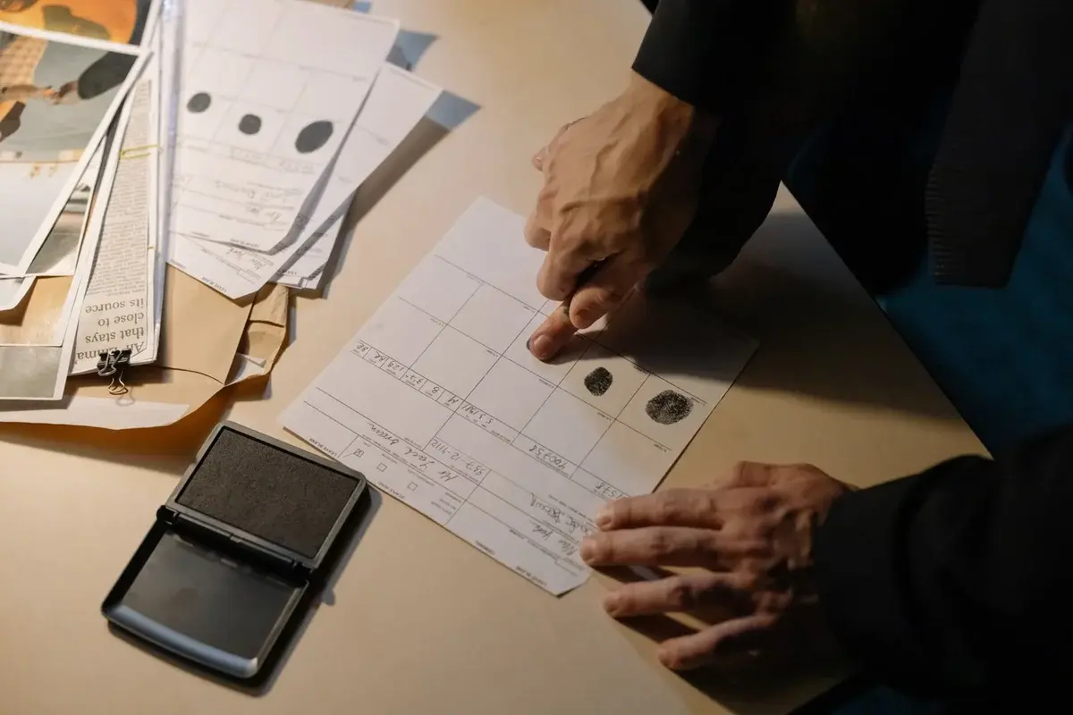 Hands examining fingerprint documents on a desk beside an ink pad.
