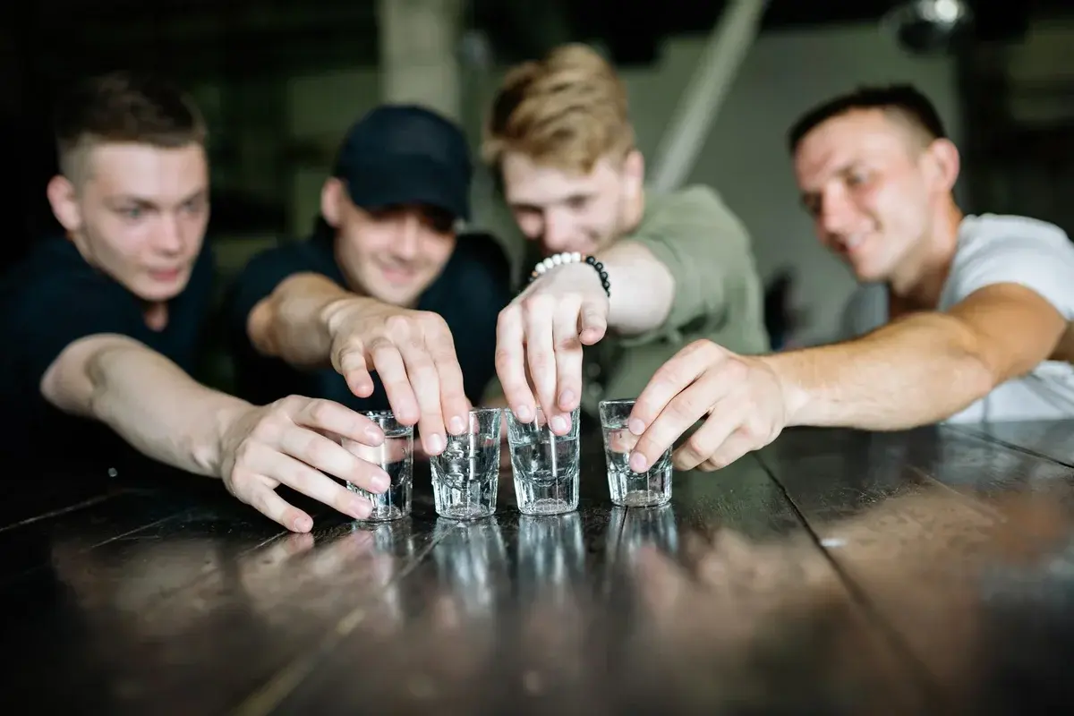 Four friends reaching for shot glasses on table indoors