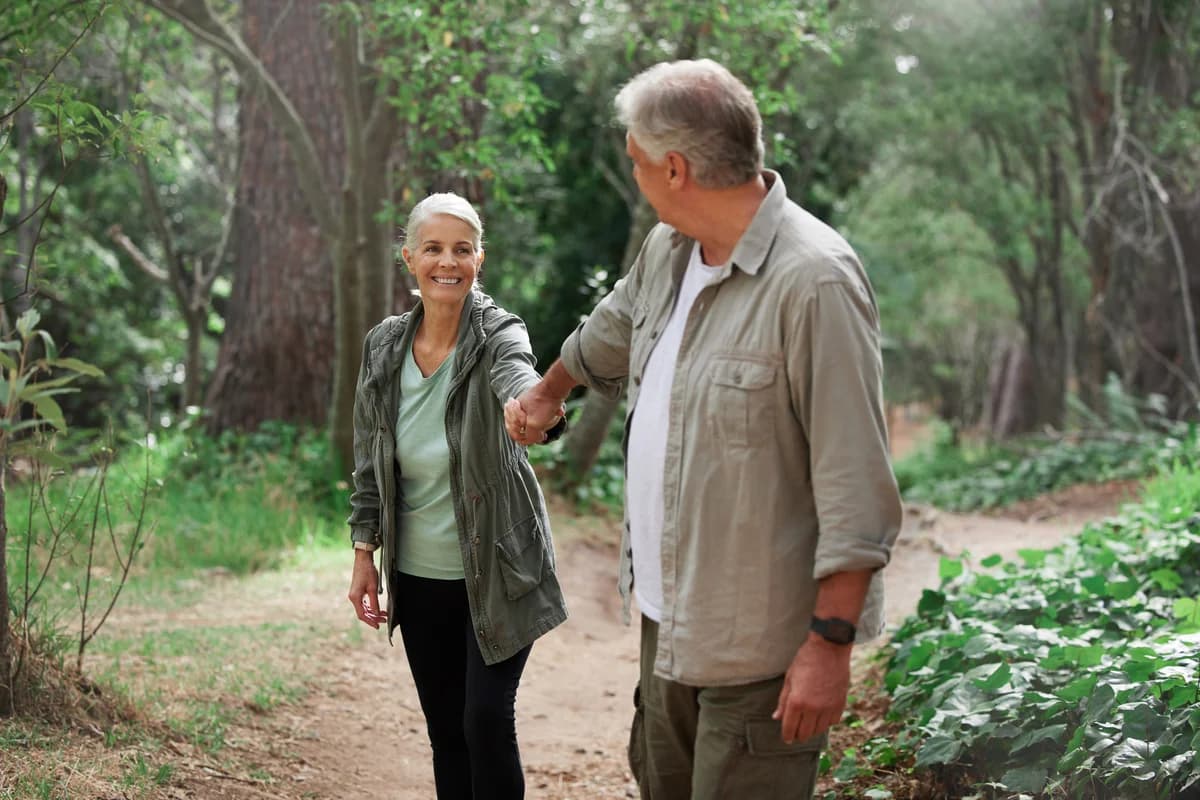 An older couple holding hands while walking in a forest.