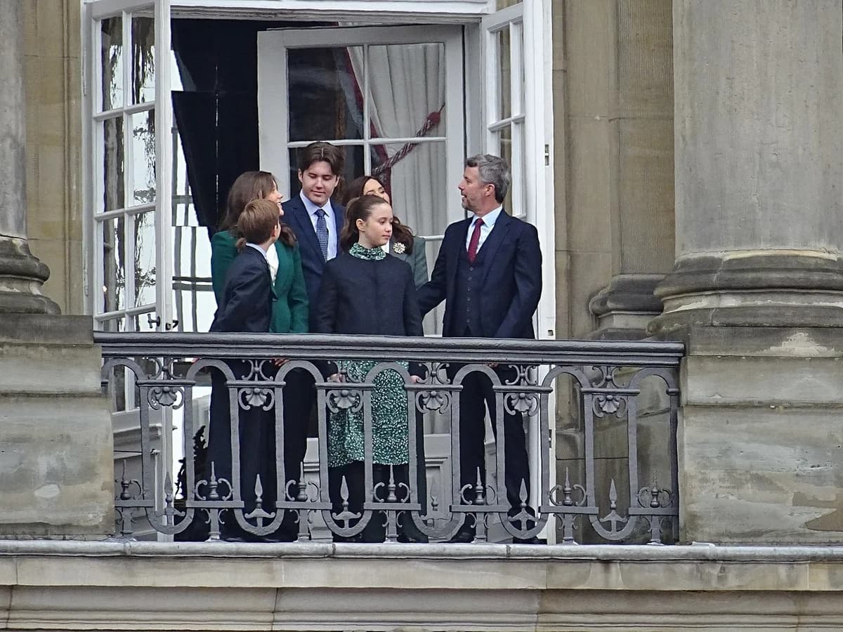 Members of the Danish royal family stand on a palace balcony and wave to the public.