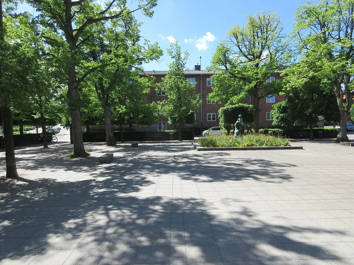 A sunny urban square with trees, a statue, and apartment buildings in Lyngby, Denmark.