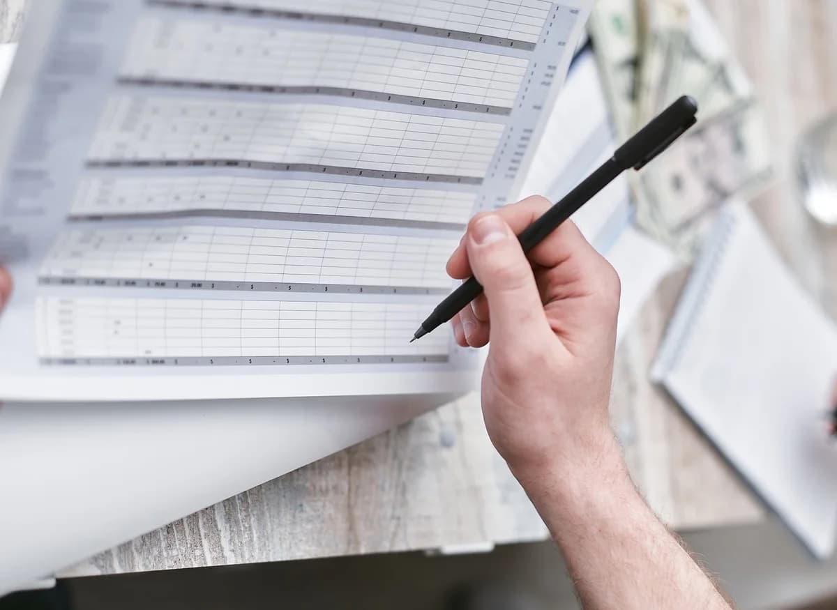 Hand with pen reviewing financial document and visible cash