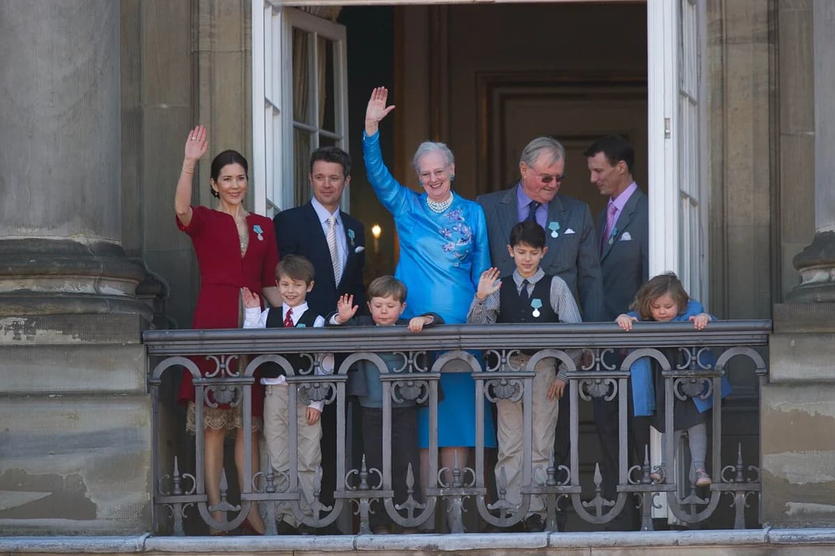 Queen Margrethe II and members of the Danish royal family wave from a palace balcony.