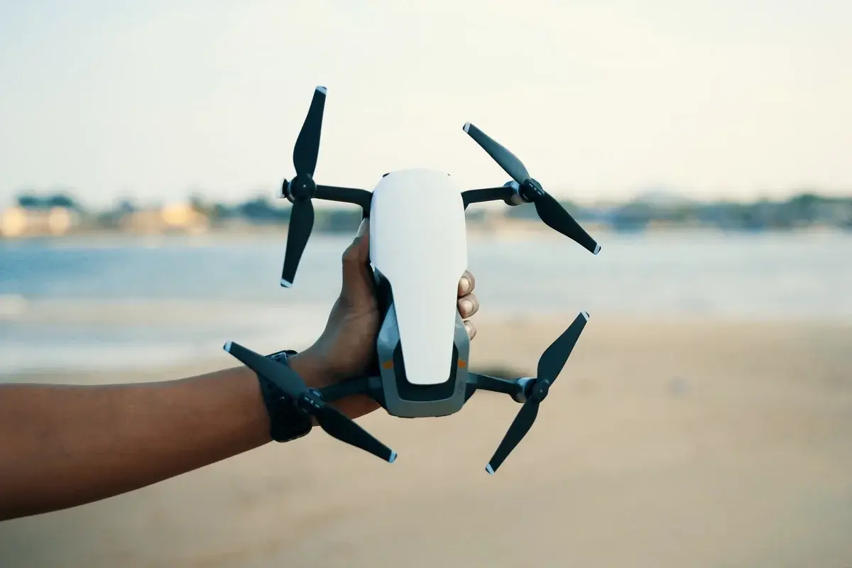 A hand holding a drone on a beach.