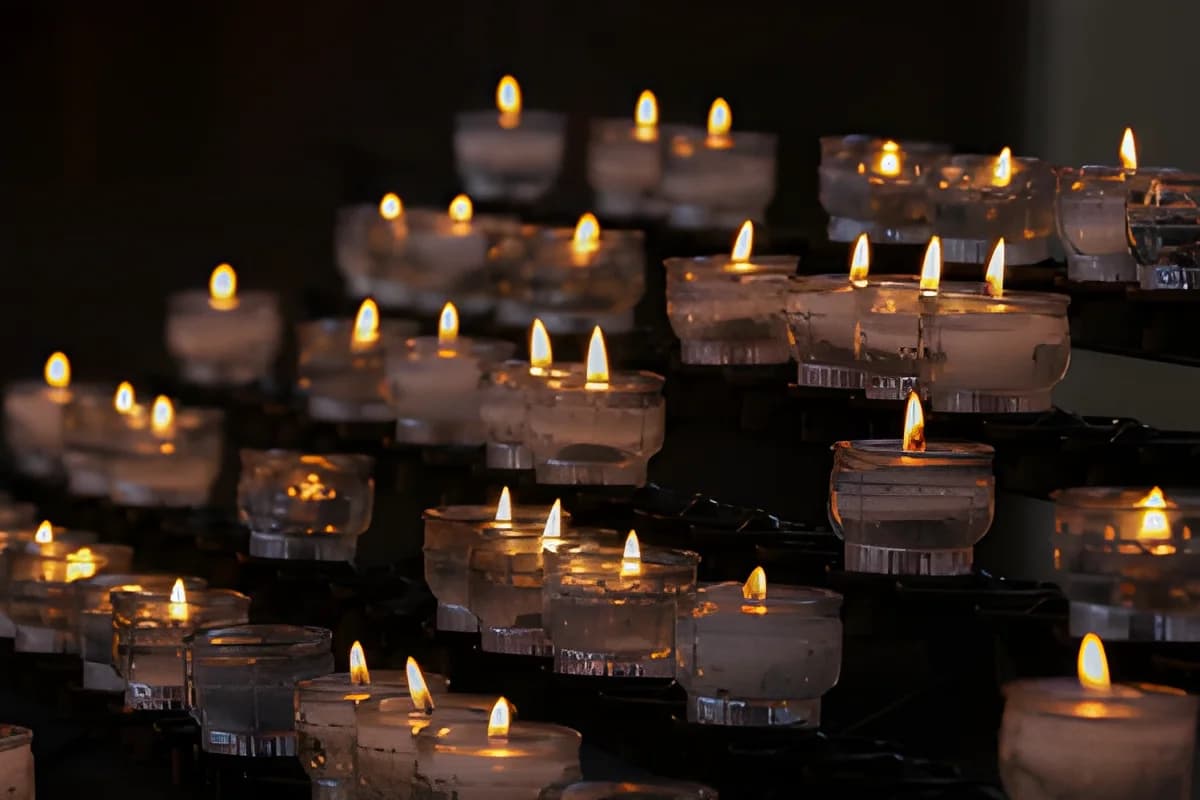 Rows of lit candles in glass holders glowing in a dark setting.