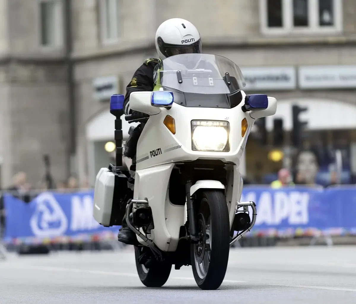 A Danish police motorcycle with flashing lights on a city street.