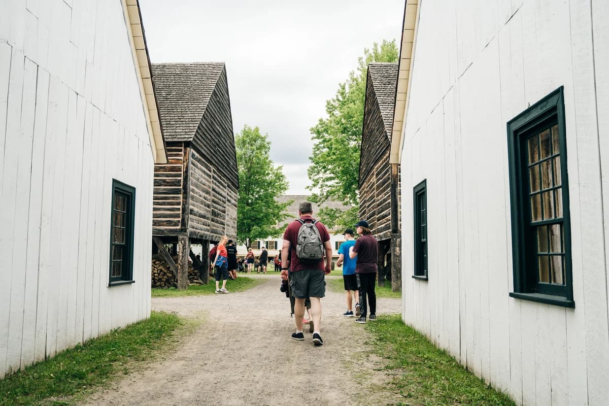 People walking between historic wooden buildings at Fort William Historical Park.