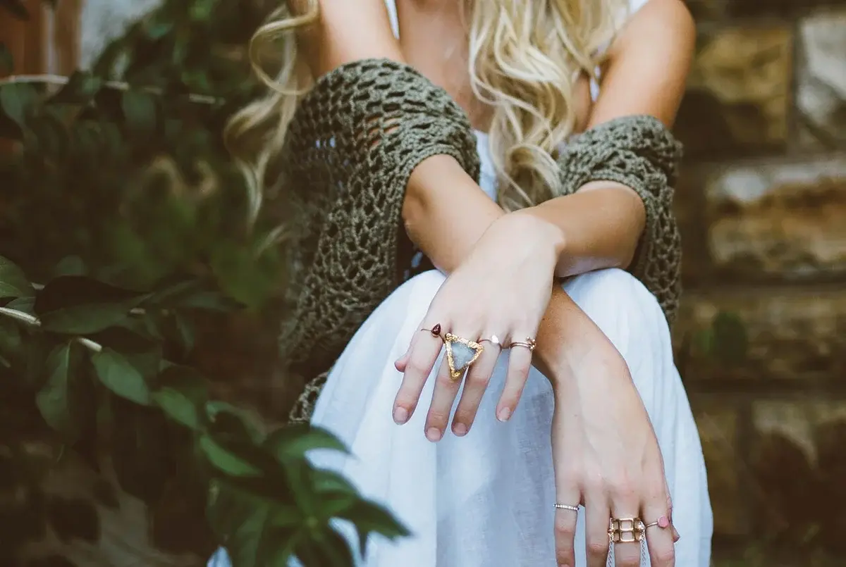 Close-up of a blonde woman sitting outdoors in a white dress and knitted shawl.
