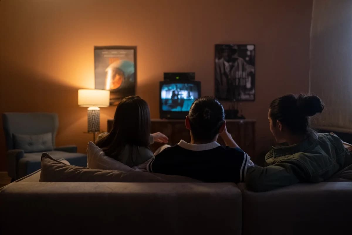 Three people sitting on a couch watching TV