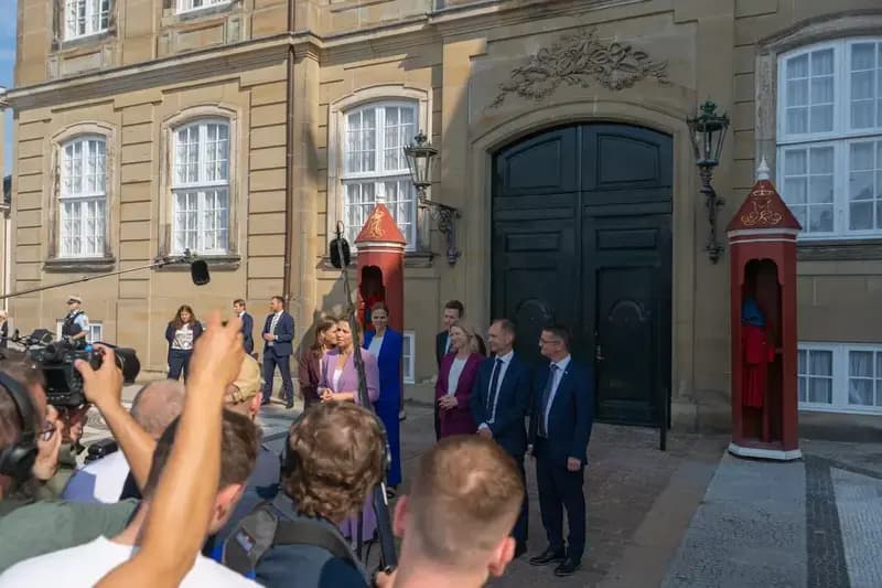 Danish politicians speaking at a press conference outside a government building with media present