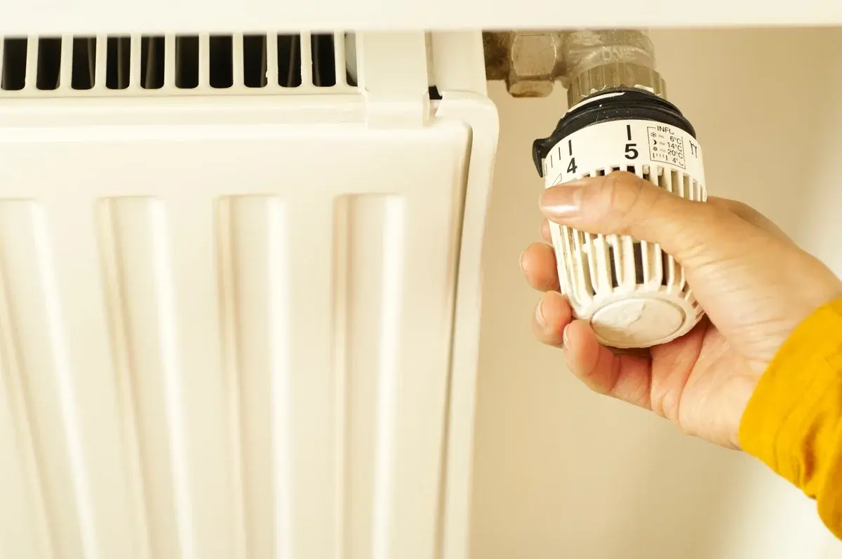 A hand turning a radiator thermostat on a white radiator.