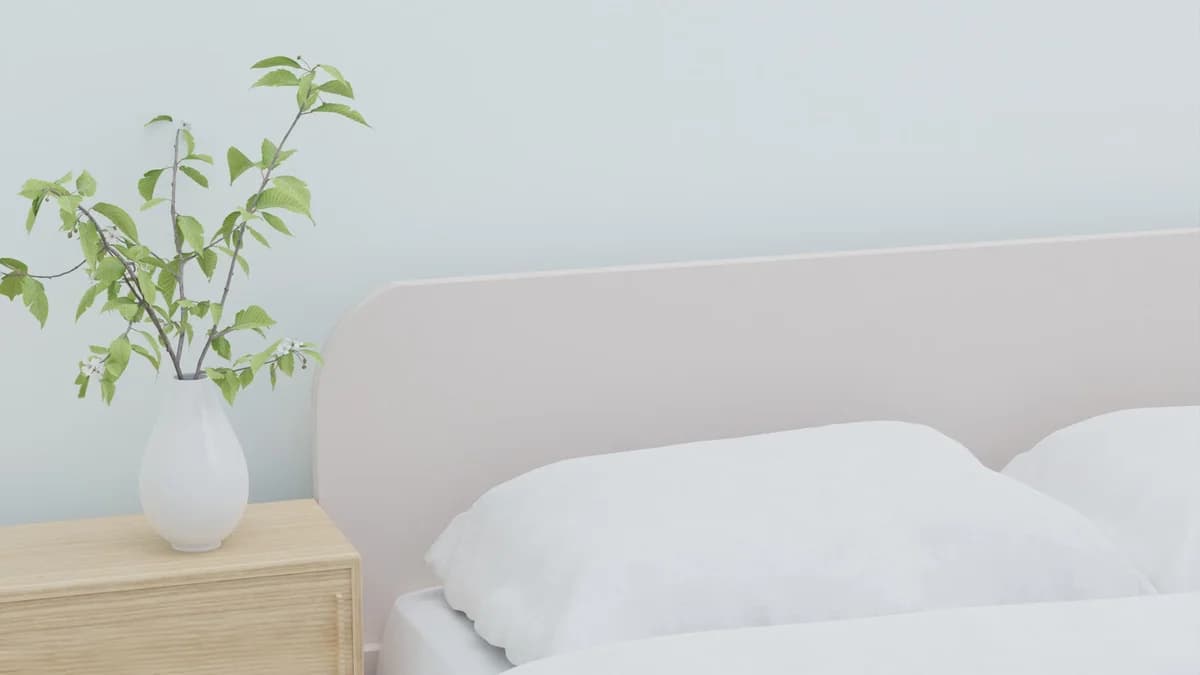 A bright bedroom with white bedding and a vase of green branches on a wooden nightstand.