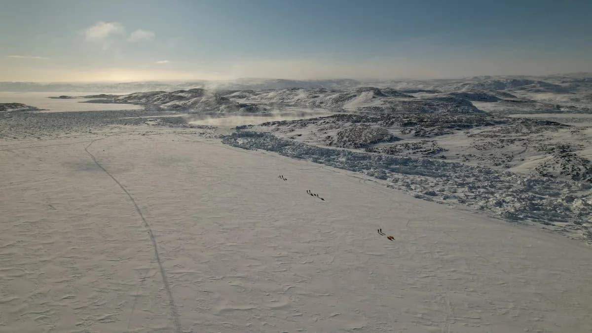 Drone view of people crossing a snowy frozen landscape in Greenland.