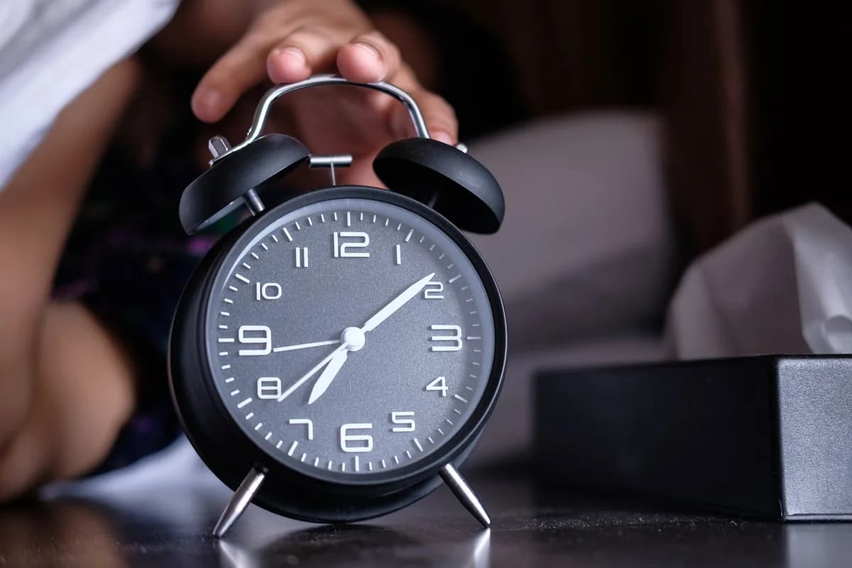 Hand reaching toward an analog alarm clock