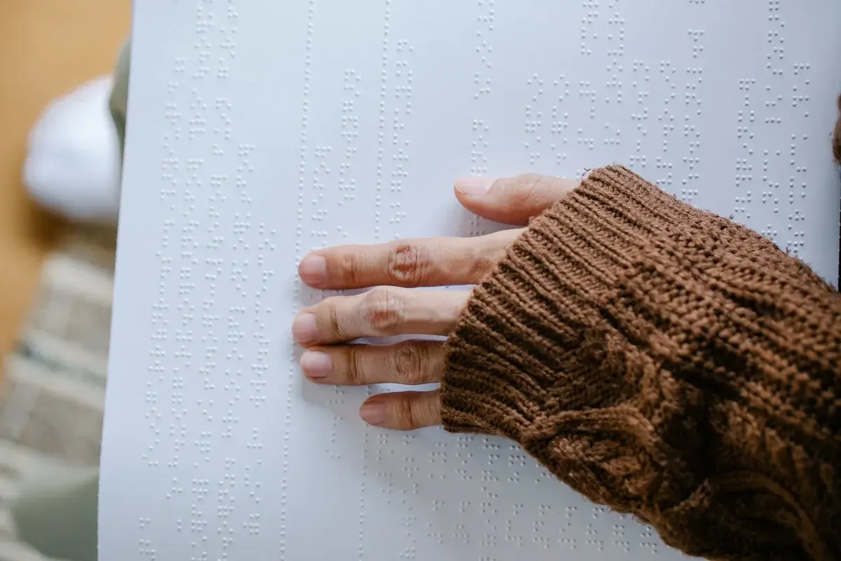 A hand touches Braille text on paper.