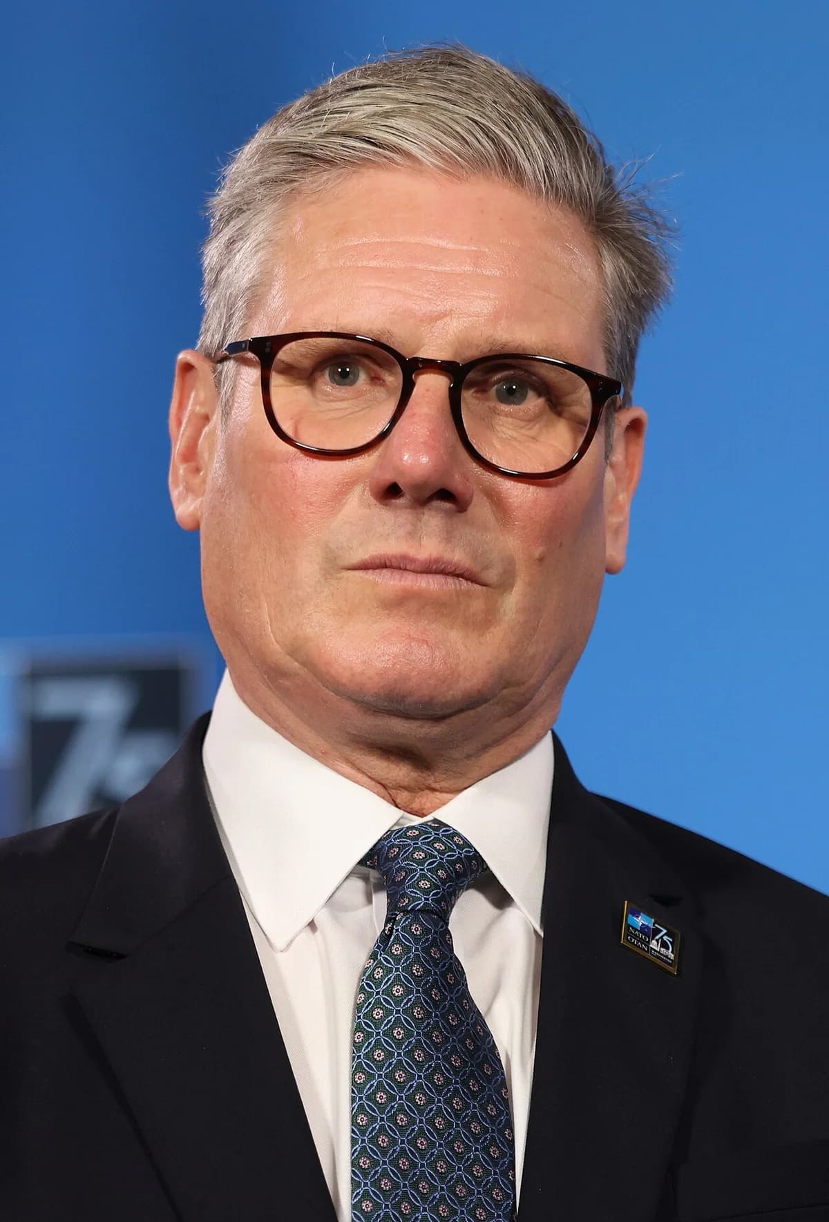 Close-up of Jens Stoltenberg in a suit and tie against a blue background.