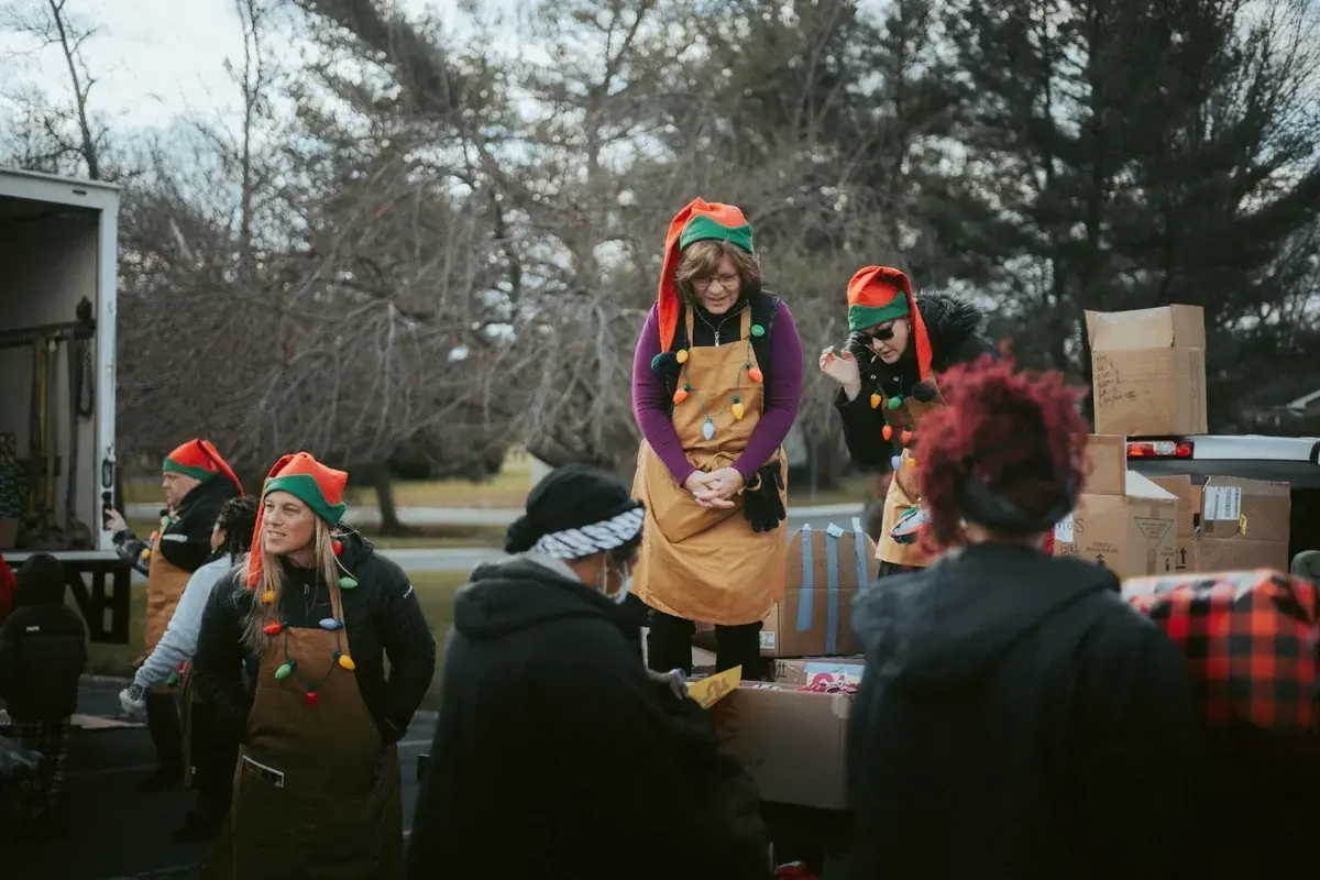 Volunteers in elf hats distribute gifts from a truck at a community event.
