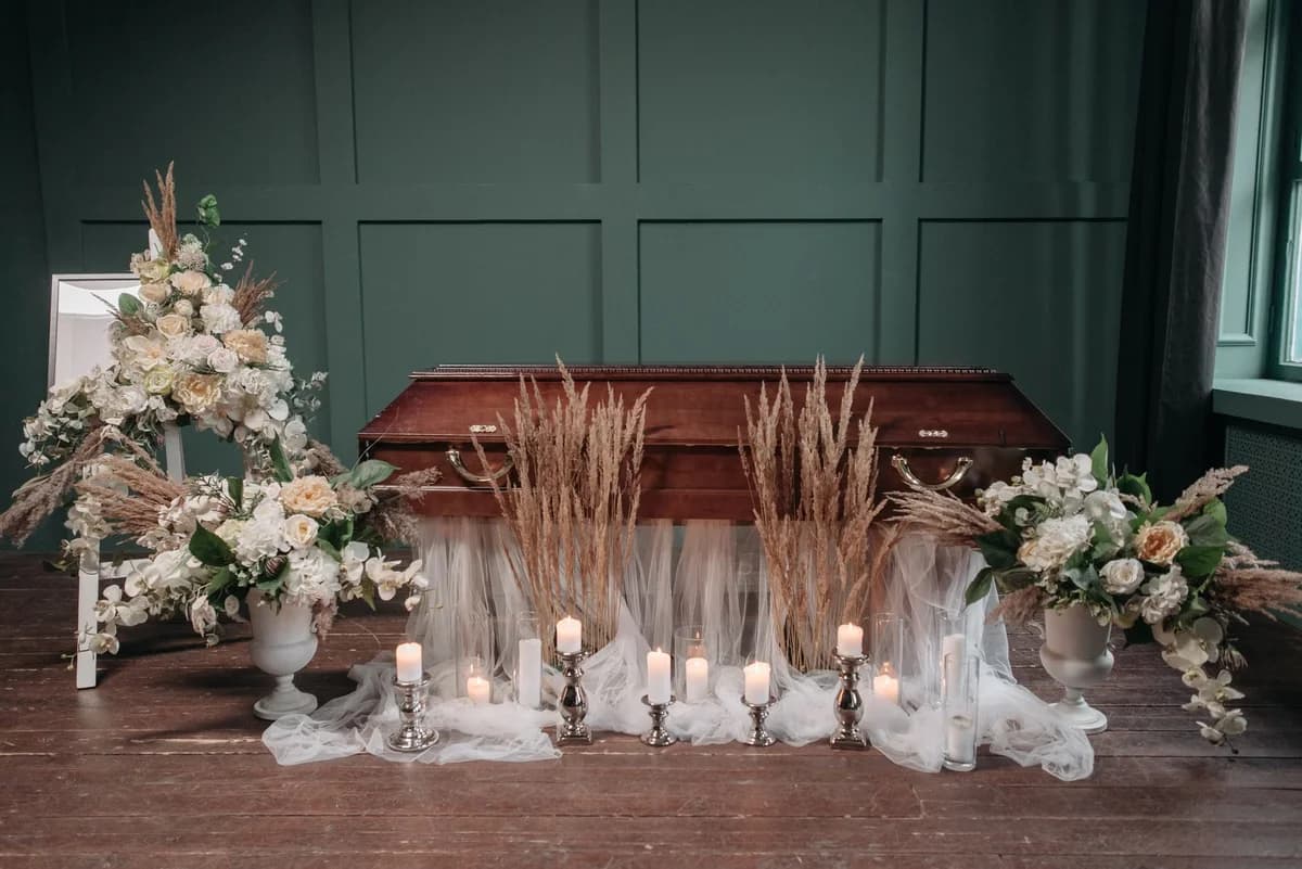 A wooden casket surrounded by candles and flower arrangements indoors.