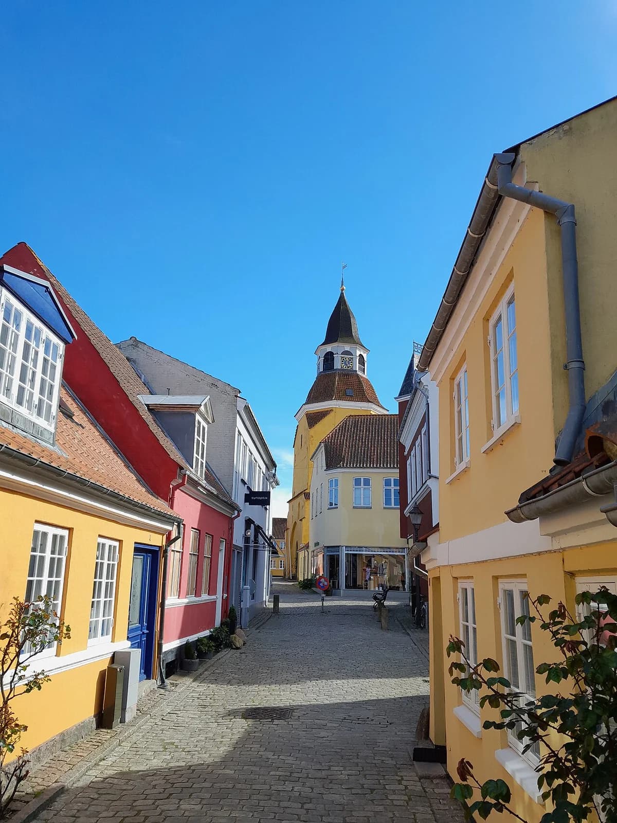 Colorful houses on a cobblestone street with a bell tower in the background.